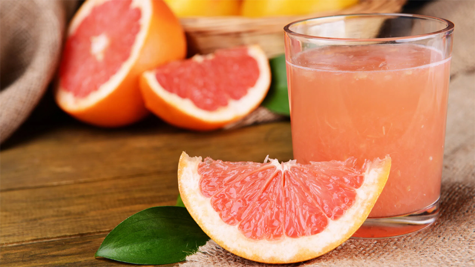 Un pahar cu suc de grapefruit langa o felie de grapefruit in prim plan.